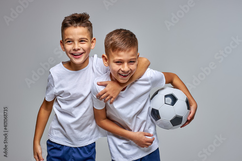 Fototapeta Naklejka Na Ścianę i Meble -  kid boys go in for soccer sport professionally, stand hugging each other, have fun, smile at camera, holding ball in hands, isolated portrait
