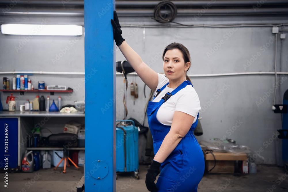 Obraz premium A woman in a blue uniform is standing in the workshop and looking at the camera