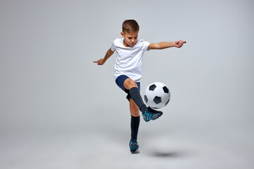 young caucasian boy with soccer ball doing flying kick isolated in studio, athletic sportive boy in uniform