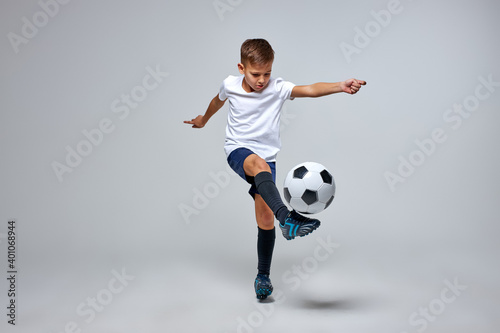 young caucasian boy with soccer ball doing flying kick isolated in studio, athletic sportive boy in uniform © Roman