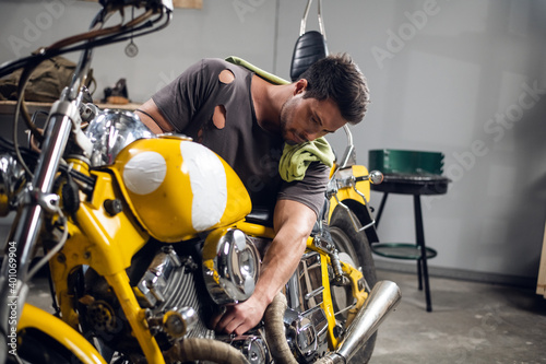 Private vehicle repair shop. Tuning a yellow chopper by a young mechanic