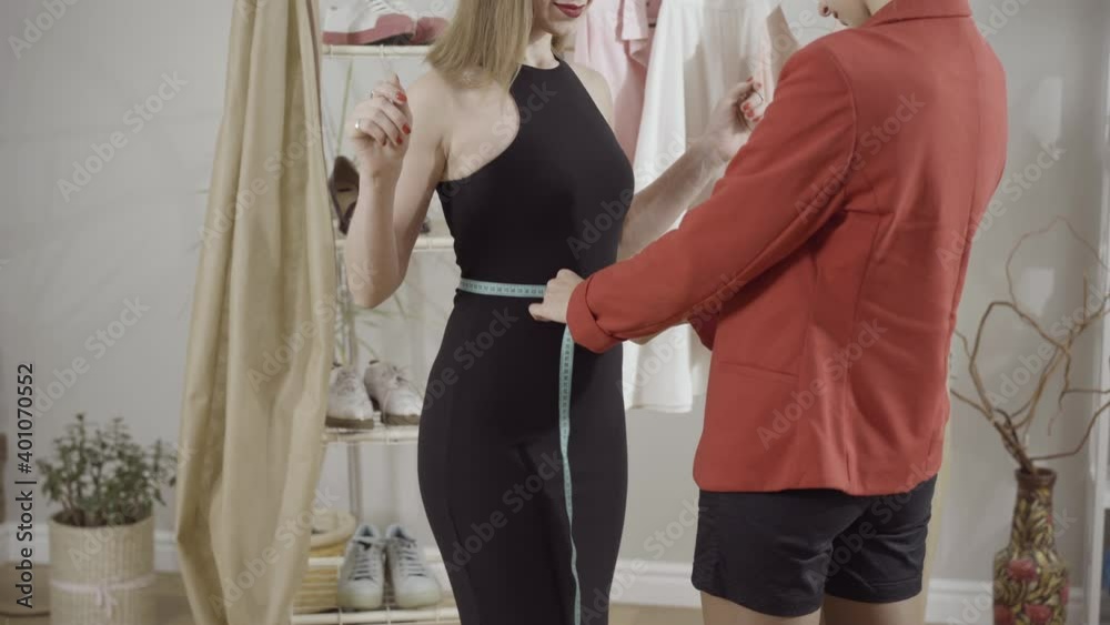 Unrecognizable seamstress measuring waist of slim elegant Caucasian woman in atelier indoors. Young professional dressmaker taking measurements for bespoke tailor-made dress.