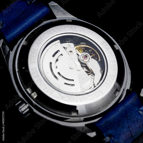 Mechanical watch movement seem from the back on a metal stainless steel glass case and blue strap