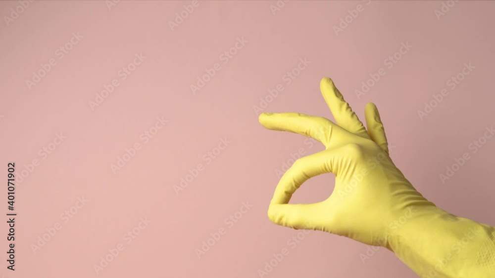 Hand in yellow rubber cleaning glove showing gesturing okay on pink background