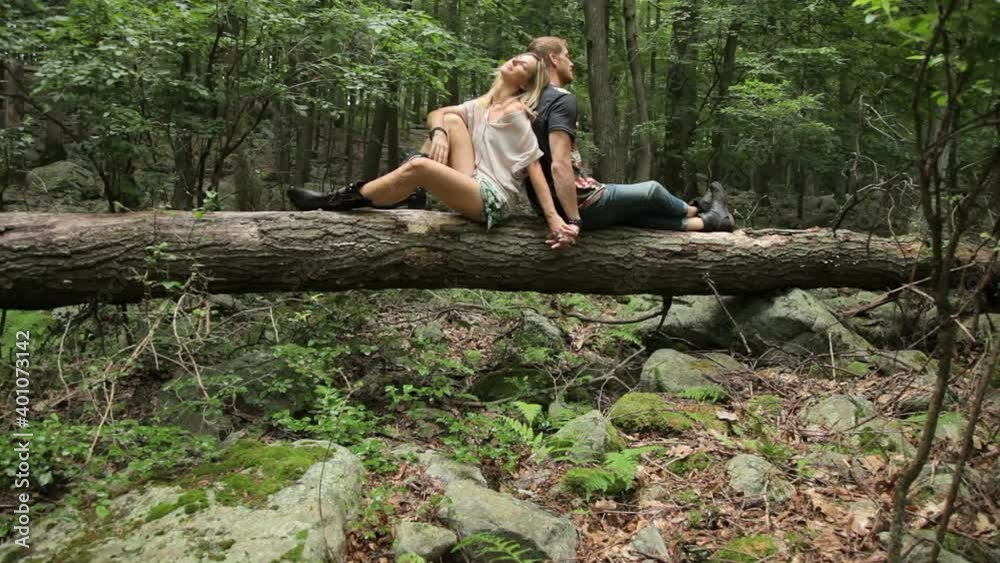 Couple sitting back to back holding hands on log in forest Couple sitting back to back holding hands on log in forest