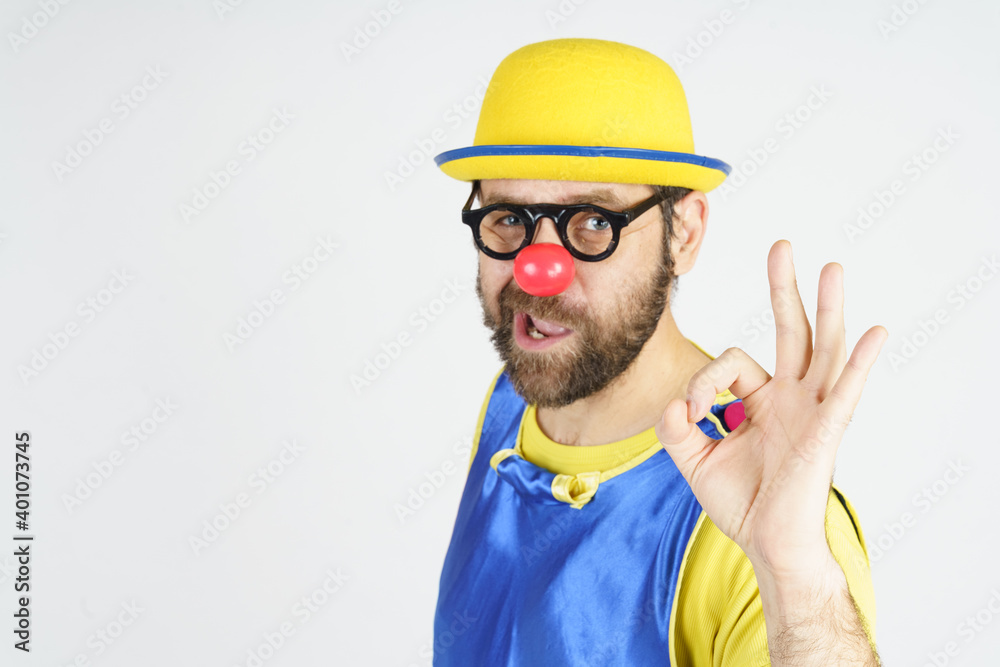 A clown in a bright blue and yellow suit, glasses and a hat shows an OK gesture A clown in a bright blue and yellow suit, glasses and a hat shows an OK gesture