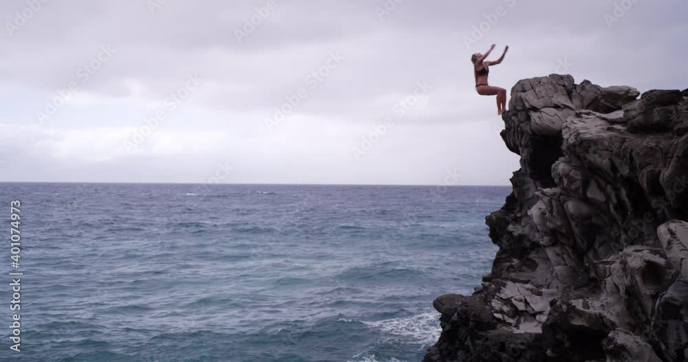 Caucasian woman doing back flip off cliff into ocean on Maui