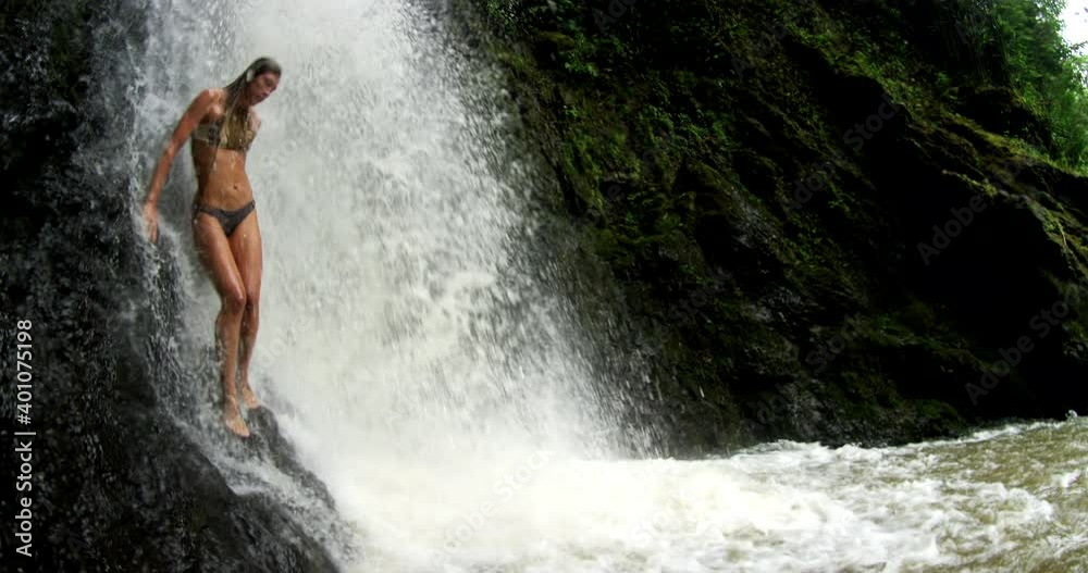 Smiling Caucasian woman standing under a waterfall Smiling Caucasian woman standing under a waterfall