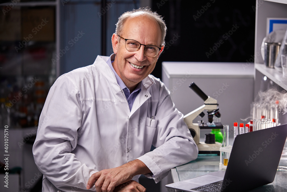 researcher in medical suit posing at vamera in laboratory, successful scientist work on laptop, with test tubes on table, smiling researcher in medical suit posing at vamera in laboratory, successful scientist work on laptop, with test tubes on table, smiling