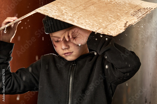 Tablou pe pânză homeless child use cardboard so as not to get wet, while raining outdoors, he is