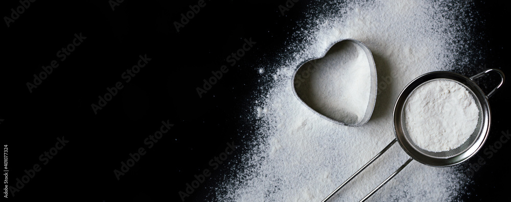 a heart made with flour and a sieve on black background with copy space a heart made with flour and a sieve on black background with copy space