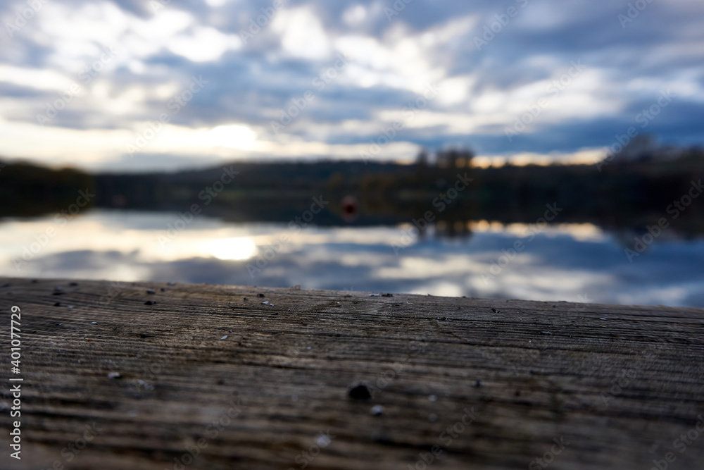 A wood plank at ta lake pond during the sunset and sun and clouds reflecting in the water