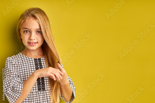 smiling girl with long blond hair isolated over green background, girl touch her chic hair and look at camera, she enjoy the silkiness of her beautiful straight hair