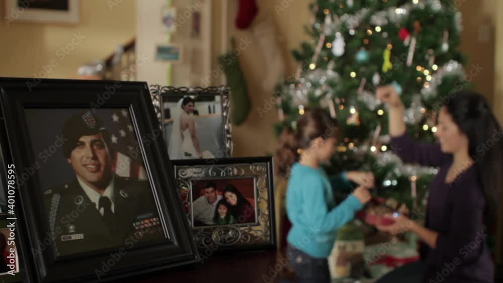 Mother and daughter decorating Christmas tree with framed portrait of father in military uniform