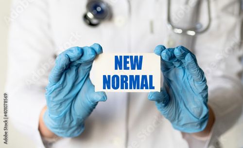 A medical worker in gloves holds a card with the words NEW NORMAL. Medical concept. Covid 19 and coronavirus concept.
