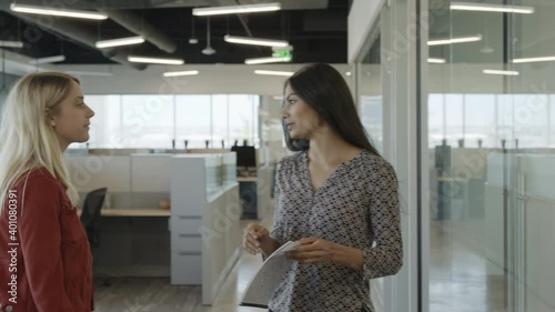 Tracking shot of businesswoman reading report and talking to passing co-worker / Pleasant Grove, Utah, United States