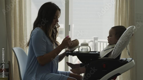 Mother feeding baby daughter in high chair near window / Bluffdale, Utah, United States photo