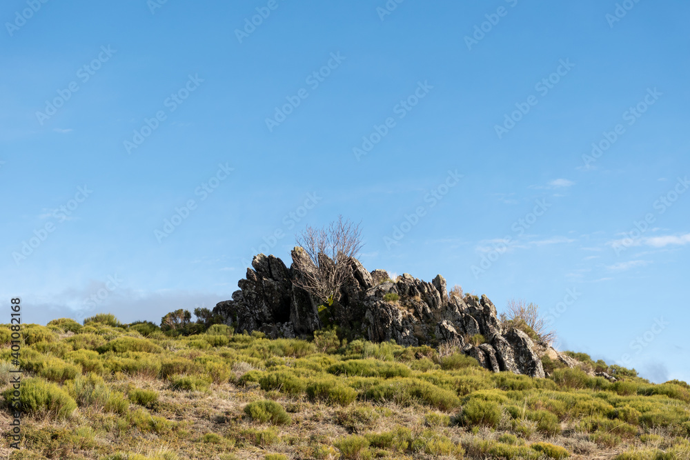 Horizontal landscape view of some rocks at the top of a mountain with a green meadow on a sunny day