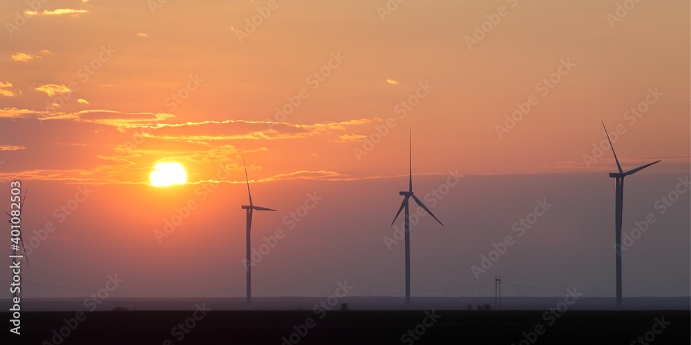 Wind turbine generating electricity in field, sunset or sunrise