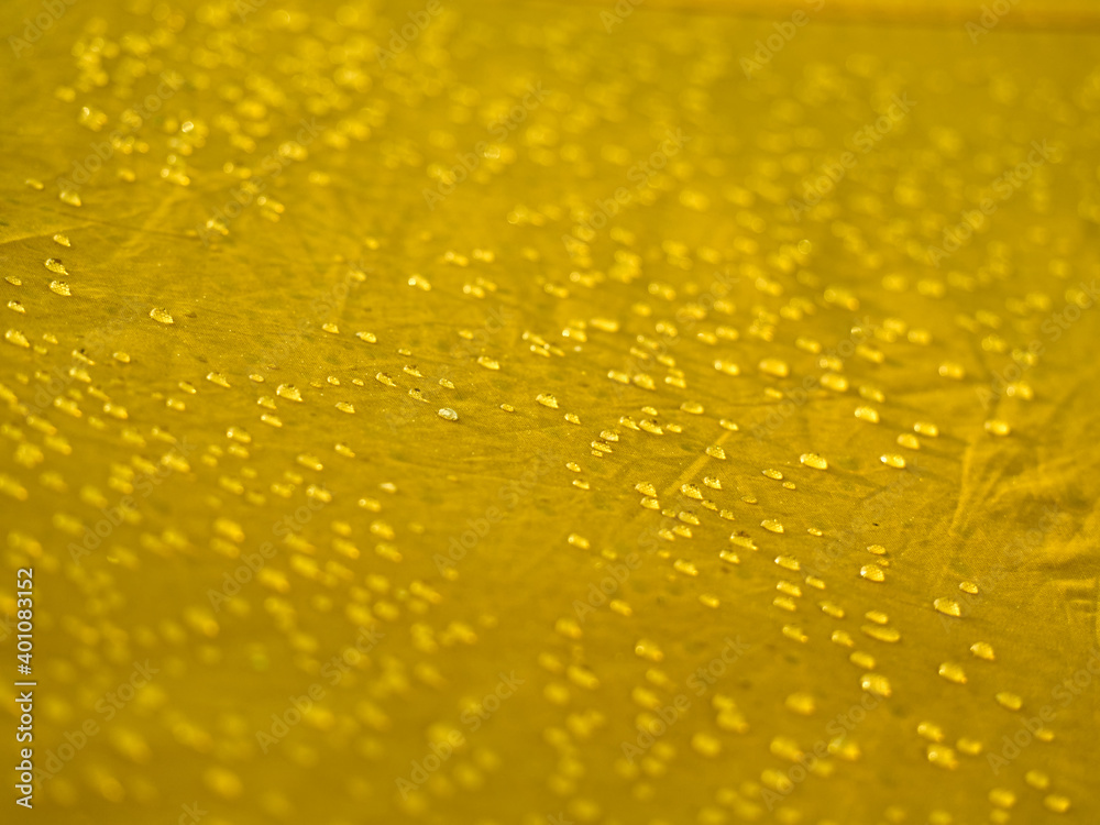 Water drops on waterproof membrane fabric. Detail view of texture of yellow synthetic waterproof cloth. Morning dew on tent.