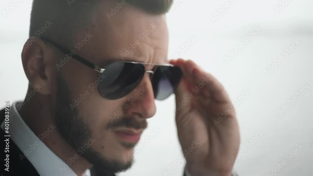 Close up of bearded handsome businessman in suit puts on his sunglasses Close up of bearded handsome businessman in suit puts on his sunglasses
