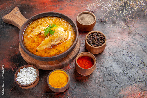 bottom view chicken soup in wooden bowl on chopping board and different spices on dark red background with free space