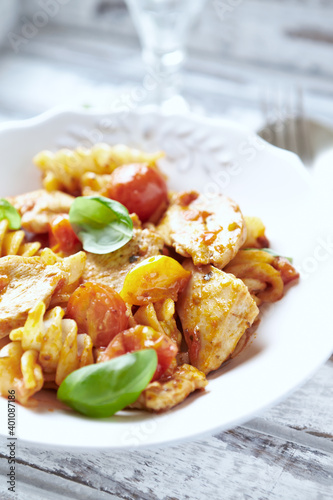 Pasta with chicken breast, cherry tomatoes and fresh basil. Bright wooden background. Close up. 