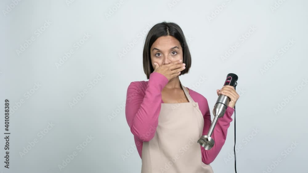 Young latin woman using hand blender covering mouth with hands. Can not speak over isolated background Young latin woman using hand blender covering mouth with hands. Can not speak over isolated background