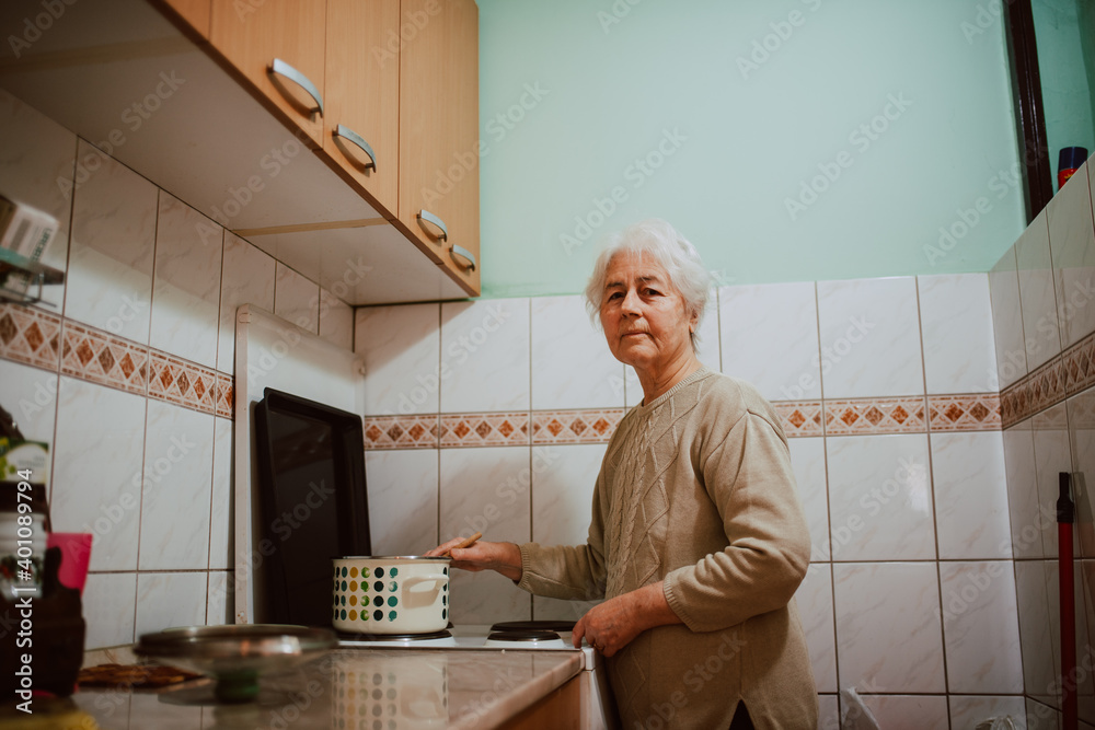 Caucasian grandmother cooking lunch in the kitchen. A gray-haired retired woman next to a kitchen stove Caucasian grandmother cooking lunch in the kitchen. A gray-haired retired woman next to a kitchen stove