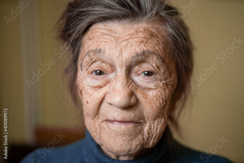 90 year old cute elderly woman with gray hair and wrinkles face, wearing sweater, portrait large, smiling and looking joyfully, background of room. Theme long-liver and aging, old people in good mood