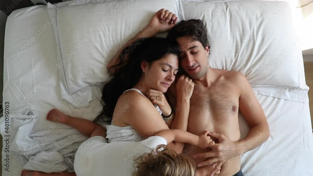 Casual parents in bed with infant baby. Mom and dad in morning bed with toddler. Top view Casual parents in bed with infant baby. Mom and dad in morning bed with toddler. Top view