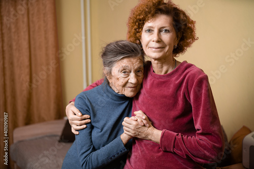 Elderly old cute woman with Alzheimer's very happy and smiling when eldest daughter hugs and takes care of her, at home on sofa. Theme aging and parenting, family relationships and social care oldest