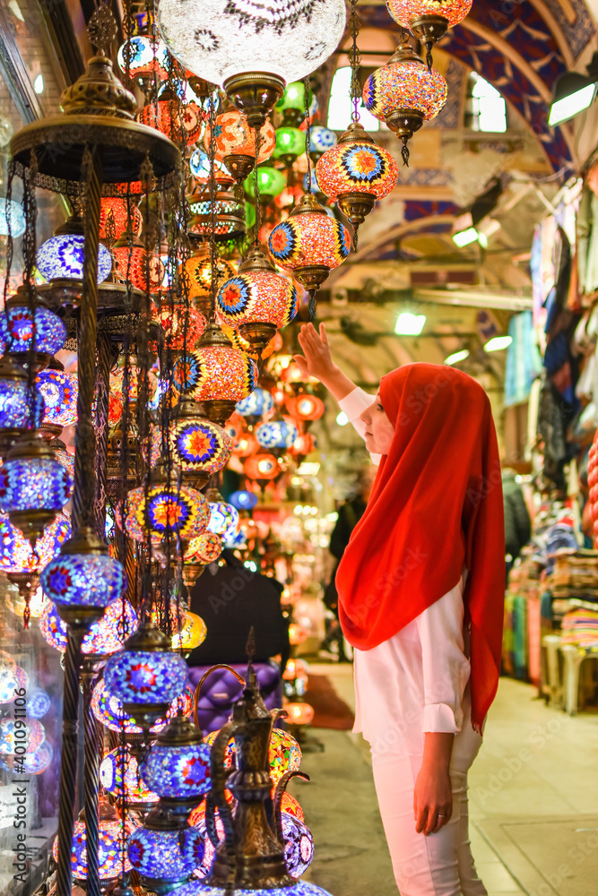 Young pretty tourist Muslim woman with red scarf looking on Traditional Turkish lamps in souvenir shop. Woman in hijab shopping in the Grand Bazar. Shopping tour.