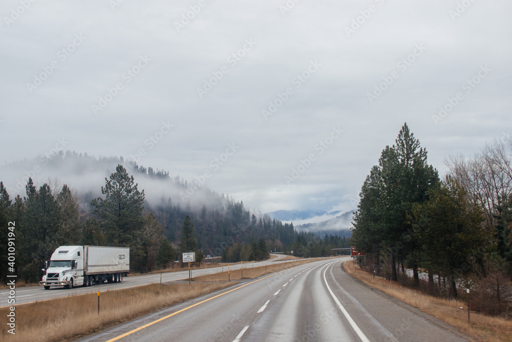 Highway with road signs on the sides among high mountains in the clouds in winter, along which trucks and cars travel. Idaho, USA, 12-5-2020 Highway with road signs on the sides among high mountains in the clouds in winter, along which trucks and cars travel. Idaho, USA, 12-5-2020