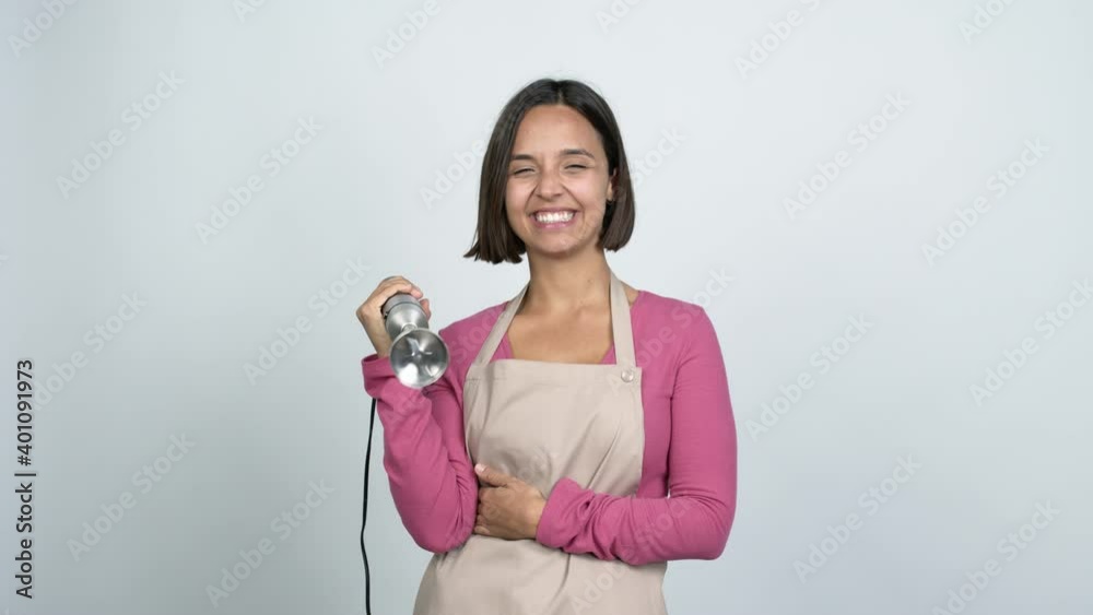 Young latin woman using hand blender smiling a lot while covering mouth over isolated background Young latin woman using hand blender smiling a lot while covering mouth over isolated background
