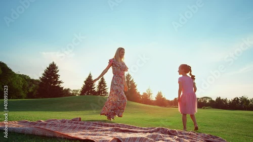 Happy mother dancing with daughter on grass. Girl doing cartwheel in park.