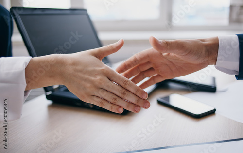 Bild auf Leinwand Employees at work shake hands at the table and a laptop in the background