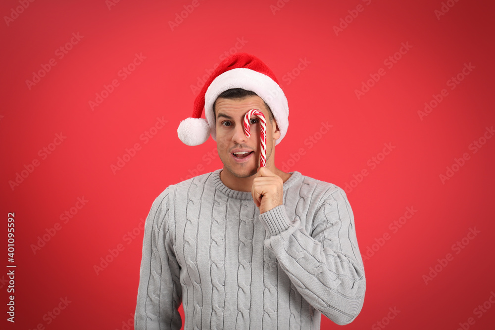 Handsome man in Santa hat holding candy cane on red background Handsome man in Santa hat holding candy cane on red background