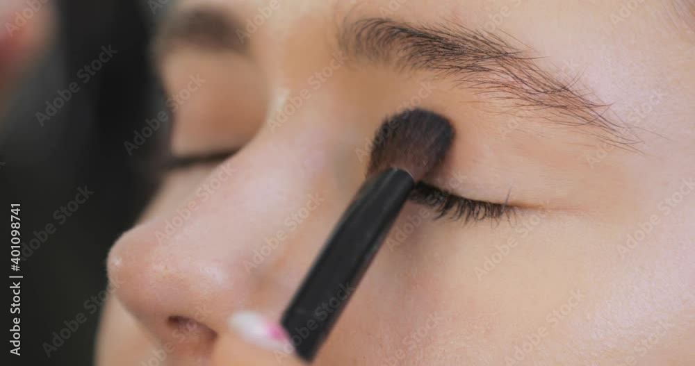Stylist visagist is doing makeup for young woman. Professional makeup artist is applies eye shadows to the upper eyelid of model eyes using brush, closeup view. Beauty industry concept. Stylist visagist is doing makeup for young woman. Professional makeup artist is applies eye shadows to the upper eyelid of model eyes using brush, closeup view. Beauty industry concept.