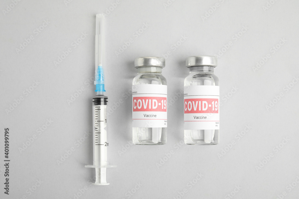 Vials with coronavirus vaccine and syringe on light background, flat lay Vials with coronavirus vaccine and syringe on light background, flat lay