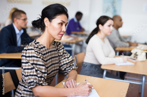 Portrait of focused young adult female sitting at desk studying in classroom with colleagues