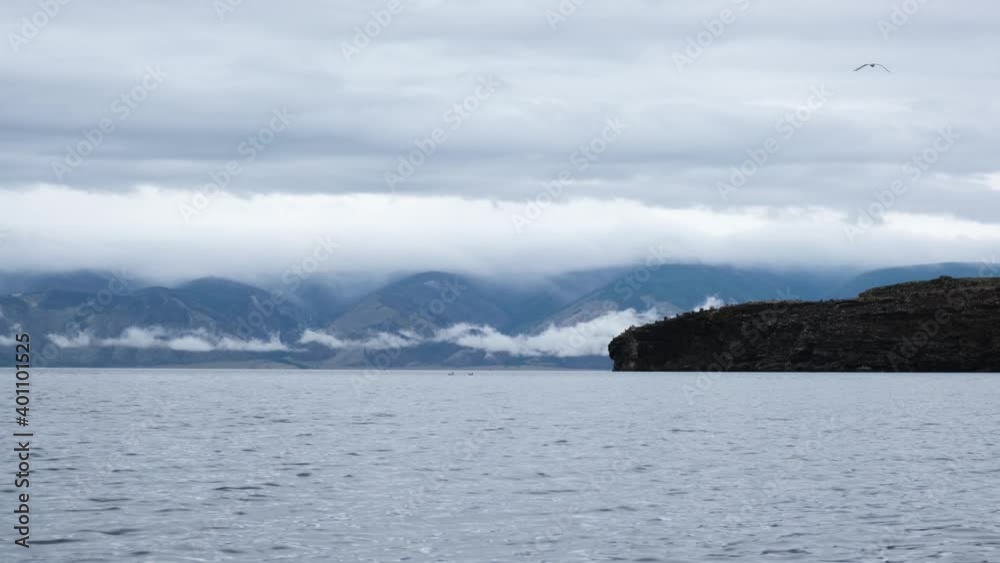 Morning Lake Baikal after rain, with blue water and mountains in dramatic low clouds and fog. A seagull is flying by. Morning Lake Baikal after rain, with blue water and mountains in dramatic low clouds and fog. A seagull is flying by.