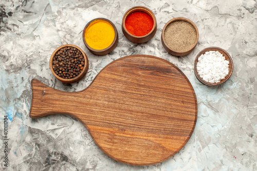 Top view of different spices necessary for cooking and wooden cutting board on ice background
