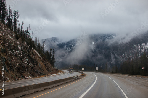 Highway with road signs on the sides among high mountains in the clouds in winter, along which trucks and cars travel. Idaho, USA, 12-5-2020