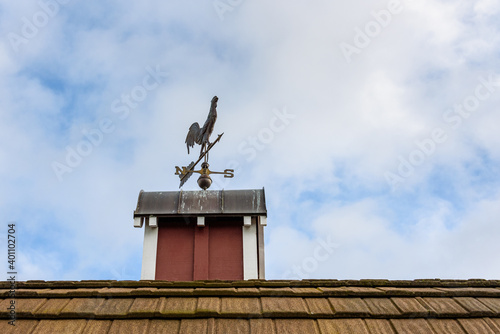 Photography Copper rooster weathervane on top of red rooftop cupola with a blue sky and whit