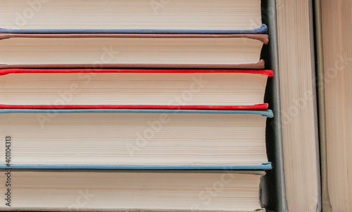 Hardcover books are stacked horizontally in a row on a bookshelf. Close- up photograph of books.