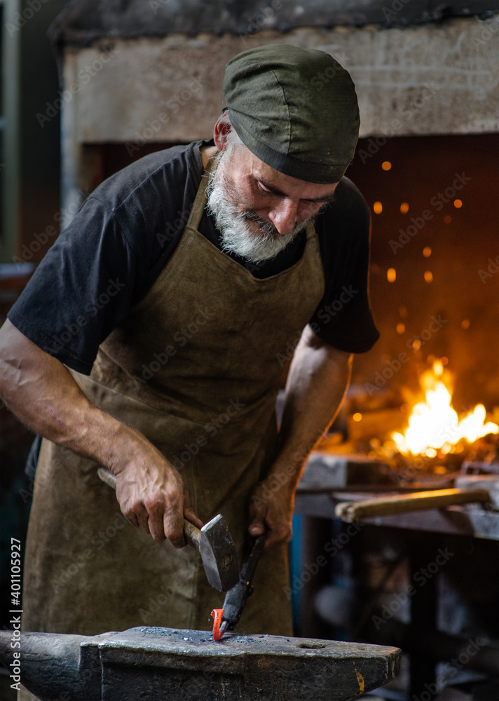 Old blacksmith working metal with hammer on the anvil in the forge Old blacksmith working metal with hammer on the anvil in the forge