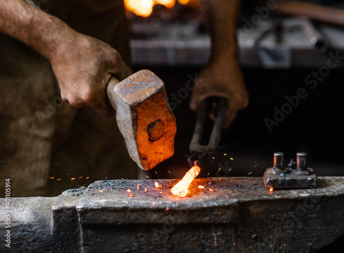 Foto Close up blacksmith working metal with hammer on the anvil in the forge