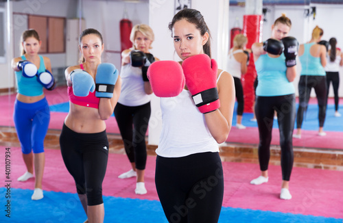 Portrait of young serious female who is training box exercises in group in sporty gym.