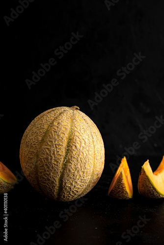 Whole melon with melon slices over black background
